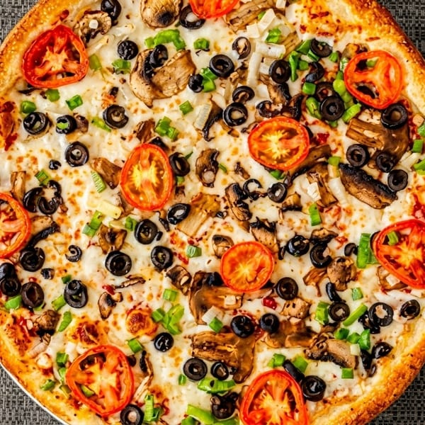 A whole vegetarian pizza with tomatoes, mushrooms, black olives, and green onions.