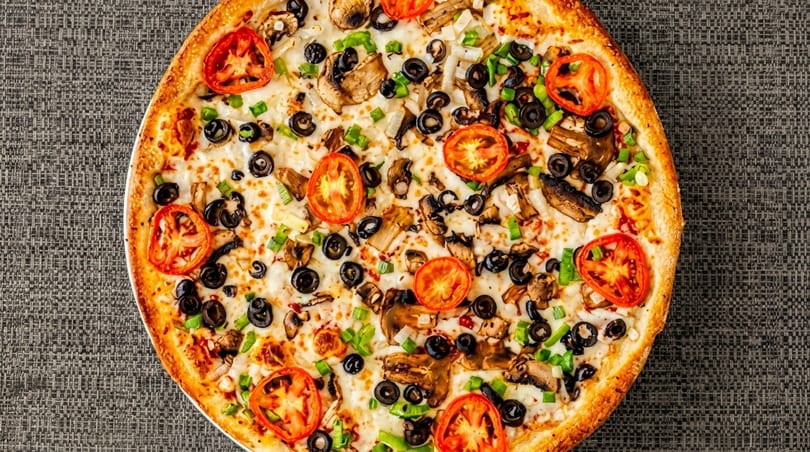 A whole vegetarian pizza with tomatoes, mushrooms, black olives, and green onions.