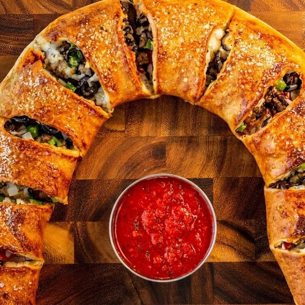 A golden-brown, crescent-shaped stromboli, sliced to reveal its savory filling, with a side of marinara sauce.