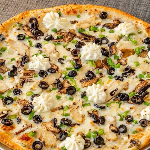 A white sauce pizza topped with chicken, mushrooms, black olives, green peppers, and dollops of ricotta cheese.